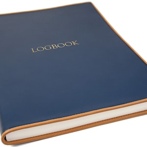 May include: A navy blue leather-bound logbook with a tan leather trim and the word "LOGBOOK" embossed in gold on the front cover.