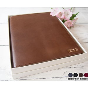 May include: A brown leather journal with gold lettering that says "SDLF" in a white box. The journal is on a wooden surface.