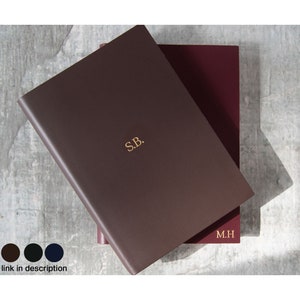 May include: Two brown leather journals with gold lettering. The top journal has the initials "S.B." and the bottom journal has the initials "M.H."