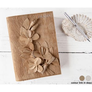 Pode incluir: Um diário de couro marrom com um design floral feito de couro. O diário tem a palavra "DIARY" gravada na capa.