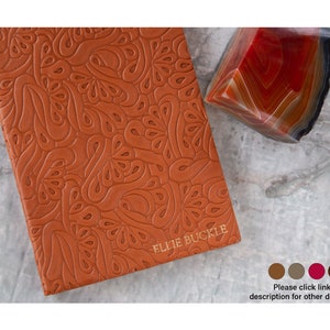 May include: A brown leather journal with an embossed paisley pattern and the text "ELLIE BUCKLE" in gold lettering.