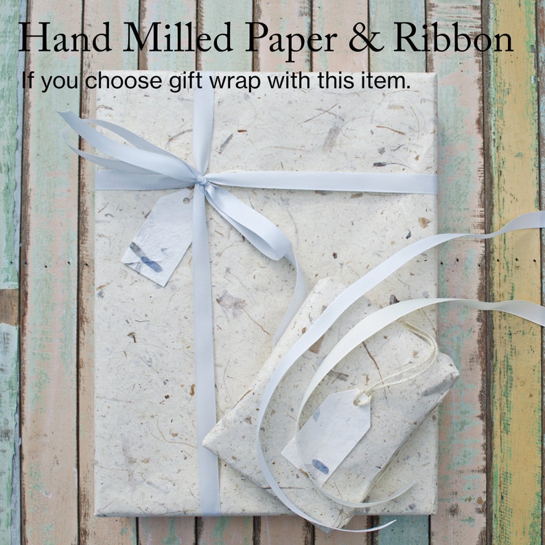 Puede incluir: Un regalo envuelto en papel blanco hecho a mano con una cinta blanca y dos etiquetas de regalo blancas. El texto "Hand Milled Paper & Ribbon" est&aacute; en la parte superior de la imagen. El texto "If you choose gift wrap with this item." est&aacute; debajo del primer texto.