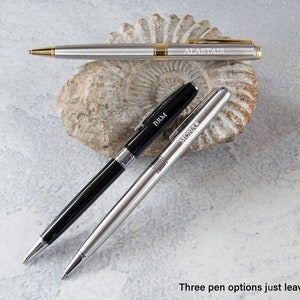 May include: Three silver pens with black and gold accents. The pens are engraved with the names "Alastair", "BRM", and "Mona".