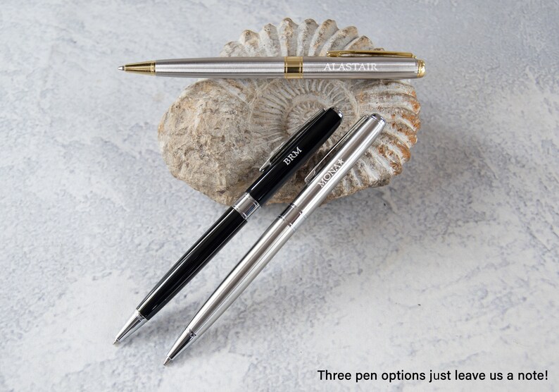 May include: Three silver pens with black and gold accents. The pens are engraved with the names "Alastair", "BRM", and "Mona".
