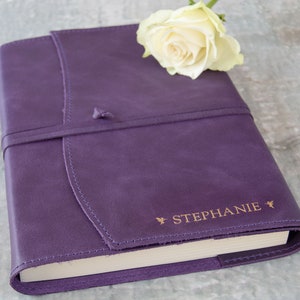May include: A purple leather-bound journal with a gold-colored inscription that reads "STEPHANIE" and a white rose on top.