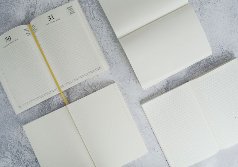 May include: Four blank notebooks, two with lined pages, one with a calendar, and one with a dotted grid pattern. The notebooks are open and lying flat on a gray textured surface.