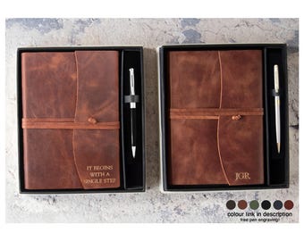 May include: Two brown leather journals with matching pens, presented in black gift boxes. One journal has the text "IT BEGINS WITH A SINGLE STEP" engraved. The other journal has the initials "JGR" engraved. The journals are tied with a leather strap.