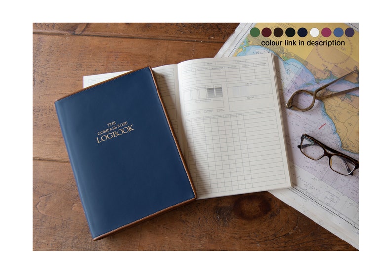 May include: A blue leather-bound logbook with gold lettering that reads "The Compass Rose Logbook". The logbook is open to a blank page with a grid pattern. A map, compass, and glasses are visible in the background.
