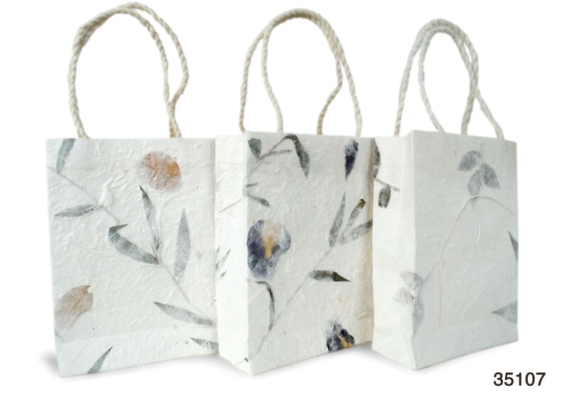K&ouml;nnte beinhalten: Drei wei&szlig;e Papier-Geschenkbeutel mit Blumendesigns und nat&uuml;rlichen Kordelgriffen. Die Beutel haben eine strukturierte Oberfl&auml;che und zeigen gepresste Blumen und Bl&auml;tter.