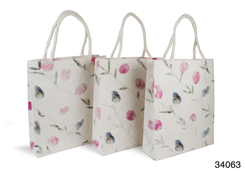 K&ouml;nnte beinhalten: Drei wei&szlig;e Papiert&uuml;ten mit rosa und blauen Blumendesigns und wei&szlig;en Kordelgriffen.