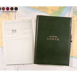 May include: A dark green logbook with the text "KINGFISHER LOGBOOK" in gold lettering. The logbook is open to reveal lined pages. A nautical chart is visible in the background.