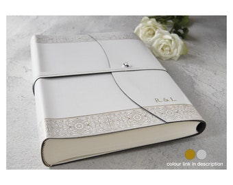May include: White leather photo album with a gold embossed design and the initials "R & L" on the front. The album has a decorative closure and a white background.