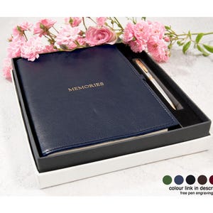 May include: A dark blue journal with the word MEMORIES embossed in gold on the cover, presented in a black and white gift box alongside a matching pen. The set is decorated with pink flowers and includes a color chart showing six options.