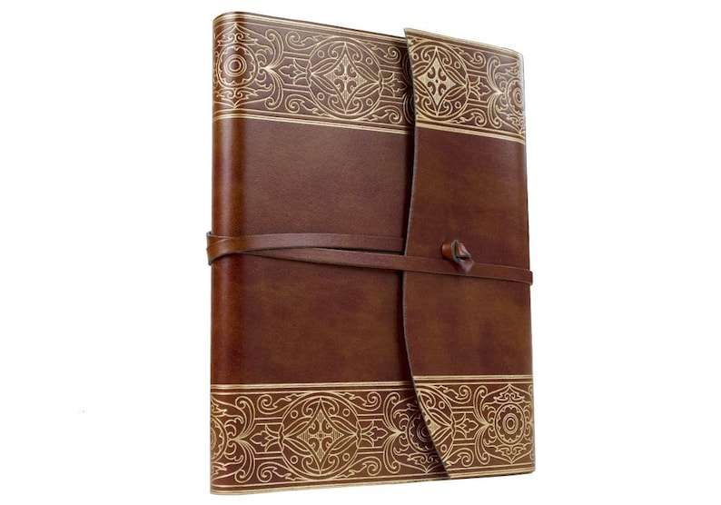 May include: A brown leather-bound journal with a gold embossed design. The journal has a strap closure and is perfect for writing or sketching.