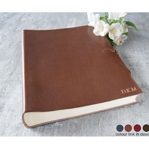 May include: A brown leather-bound journal with the initials "D.K.M." embossed on the cover. The journal is closed and lying on a light gray surface.