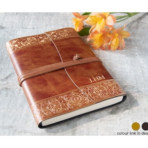 May include: A brown leather journal with gold embossed details and a leather strap closure. The journal is personalized with the initials "LHM".