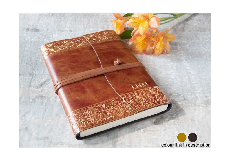 May include: A brown leather journal with gold embossed details and a leather strap closure. The journal is personalized with the initials "LHM".