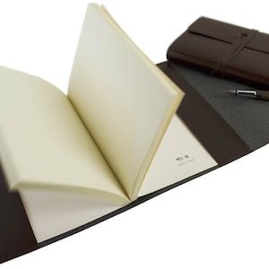 Puede incluir: Un diario encuadernado en cuero marr&oacute;n con una p&aacute;gina en blanco abierta, mostrando la inscripci&oacute;n "Made in Italy". Un bol&iacute;grafo marr&oacute;n est&aacute; sobre la cubierta.