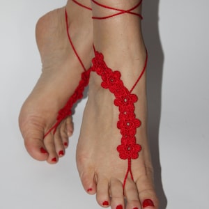 May include: Red crocheted barefoot sandals with flower accents. The sandals are tied around the ankles with red string.