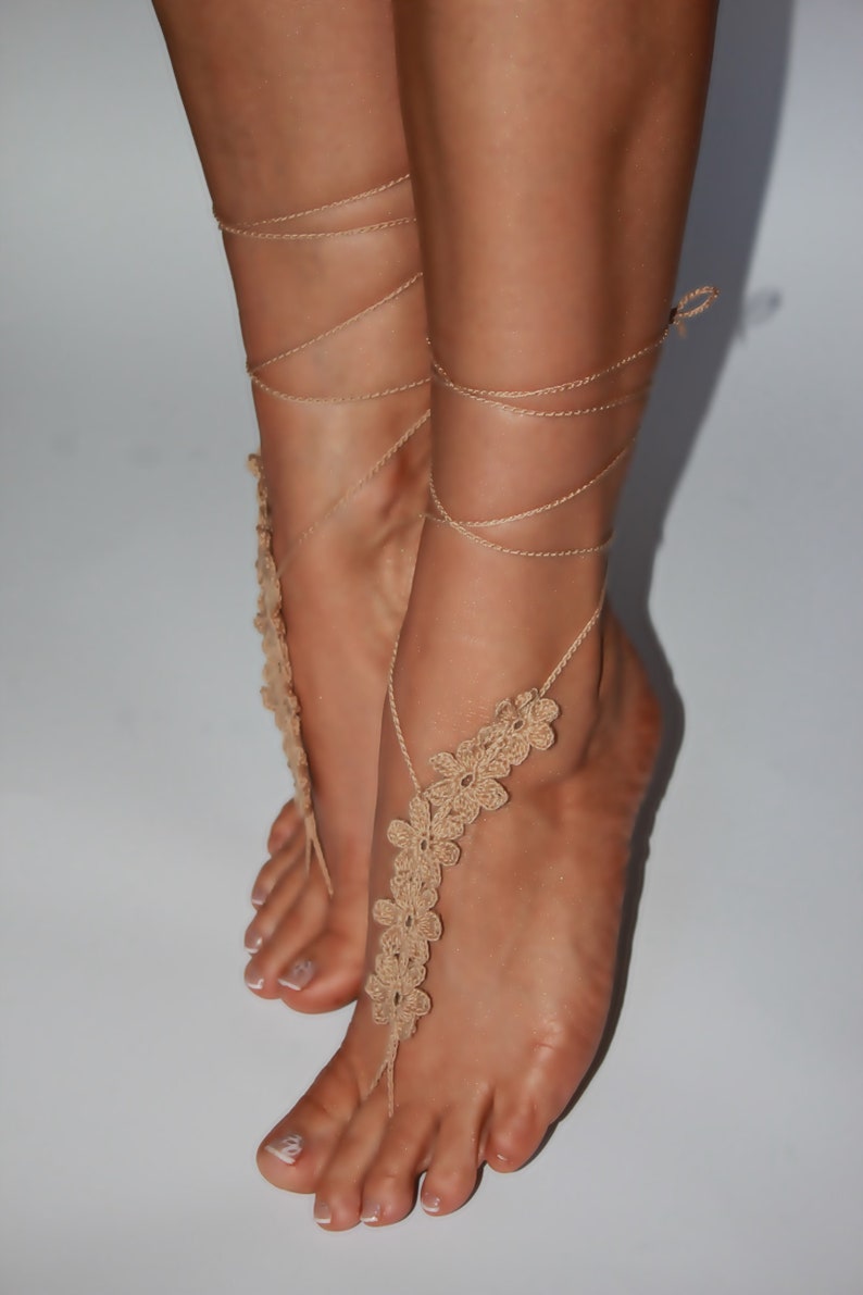 May include: Beige crocheted foot jewellery with a floral design. The jewellery is tied around the ankles with strings.