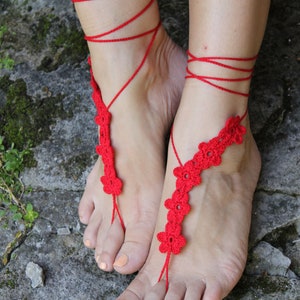 May include: Red crocheted barefoot sandals with flower accents. The sandals are tied around the ankles with red string.