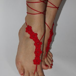 May include: Red crocheted foot jewellery with flower accents. The jewellery is tied around the ankles and feet.