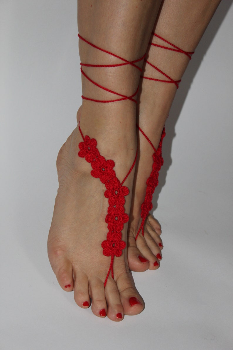 May include: Red crocheted foot jewellery with flower accents. The jewellery is tied around the ankles and feet.