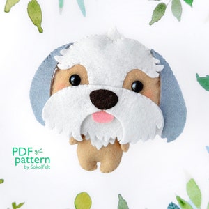 May include: A white and brown felt Shih Tzu dog with blue ears. The dog is sitting on a white background with green watercolour leaves.