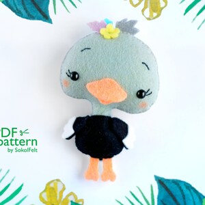 Könnte beinhalten: Ein Nähmuster aus Filz für eine süße graue und schwarze Ente mit einer gelben Blume auf dem Kopf. Das Muster heißt "PDF pattern by SokolFelt".