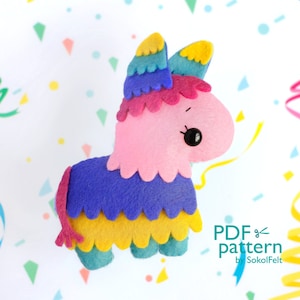 May include: A pink felt pinata shaped like a donkey with a blue, yellow, and green fringe. The pinata has a black eye and a small pink tail. The pinata is on a white background with confetti.