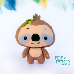May include: A brown and beige felt sloth with a smiling face, black eyes, and a green leaf on its head. The sloth is standing on a white surface. PDF pattern by SokolFelt.