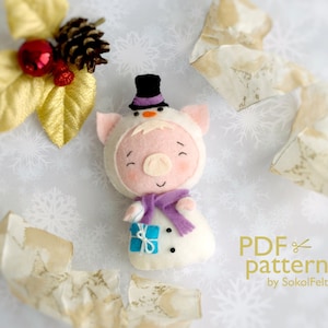 May include: A felt pig wearing a snowman costume with a purple scarf and a black top hat. The pig is holding a blue gift box with a white ribbon. The text "PDF pattern by SokolFelt" is in the lower right corner of the image.