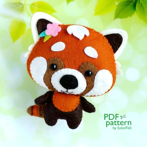 以下が含まれることがあります： 白い顔と茶色の耳を持つフェルトの赤いパンダのぬいぐるみ。おもちゃは頭に小さな花をつけており、緑と白の背景に立っています。SokolFeltによるPDFパターンです。