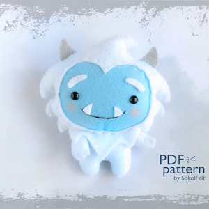May include: A blue and white felt Yeti plush toy with a friendly face. The toy is standing on a white background. PDF pattern by SokolFelt.
