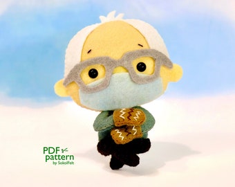May include: A felt plush toy of a person wearing glasses and a face mask. The person is holding two brown felt gingerbread cookies. The toy is made for sewing and is a PDF pattern by SokolFelt.