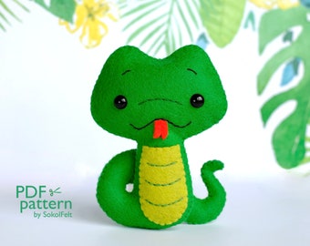 May include: A green felt snake with a yellow belly and a red tongue. The snake has large black eyes and a stitched smile. The snake is a plush toy and is sitting on a white background.
