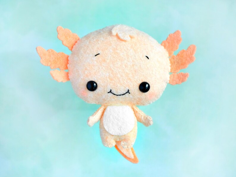 May include: A plush toy axolotl with a light orange body and a white belly. The axolotl has large, black eyes and a small, smiling mouth.