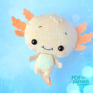 May include: A plush axolotl toy with orange gills, a light brown body, and a light green belly. The toy has black eyes and a stitched-on smile. The toy is against a light blue background.
