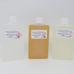 May include: Three clear glass bottles with white labels. The labels have the text "Wax & Relax" and the names of the scents: "Baby Powder", "Black Orchid", and "Unstoppable Dreams".