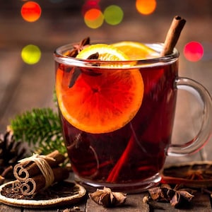 May include: A glass mug filled with red mulled wine, garnished with orange slices, cinnamon sticks, and star anise. The mug is on a wooden table with other spices and orange slices.