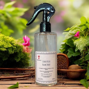 May include: A clear spray bottle with a black trigger, labelled "Linen Fresh Room Spray." The label includes text and a heart logo. The bottle contains 250ml of liquid. The background features greenery and pink flowers.