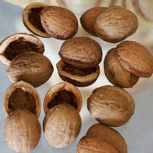 May include: A collection of walnuts, some whole and others halved, showcasing the textured, brown shells. The image highlights the natural patterns and colors of the nuts, with the empty shells revealing the inner structure.
