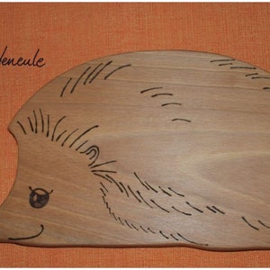 Könnte beinhalten: Ein Schneidebrett aus Holz in Form eines Igels mit einem schwarz-weißen Design. Das Brett ist aus hellbraunem Holz und hat eine glatte Oberfläche.