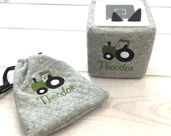 May include: A gray quilted drawstring bag and a gray cube with a green tractor design and the name "Theodor" embroidered on it.