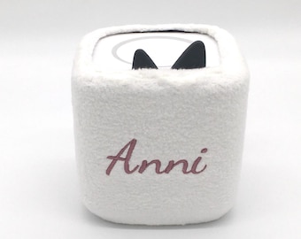 Könnte beinhalten: Ein weißer, flauschiger, quadratischer Behälter mit schwarzen Katzenohren oben. Der Name "Anni" ist in einer kursiven, malvenfarbenen Schrift auf der Vorderseite gestickt. Der Behälter hat ein weiches, strukturiertes Aussehen.