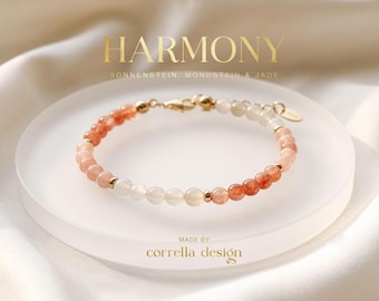 May include: A beaded bracelet featuring alternating sections of orange sunstone, white moonstone, and jade beads, accented with small gold-toned metal spacers and a lobster clasp. The text HARMONY and MADE BY corrella design are visible.