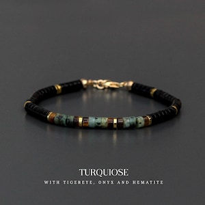 Può includere: Un braccialetto di perline nere in onice, turchese, occhio di tigre ed ematite, con dettagli e chiusura dorati. La parola "TURQUOISE" è visualizzata sotto il braccialetto, insieme al testo "WITH TIGEREYE, ONYX AND HEMATITE."