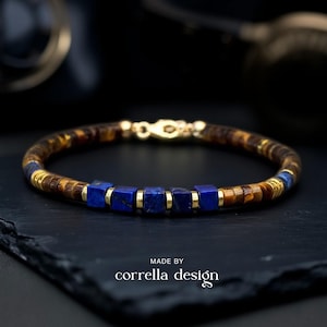 Könnte beinhalten: Armband mit braunen und goldenen Perlen, blauen quadratischen Perlen und goldfarbenen Metallakzenten. Es hat einen goldenen Verschluss. Die Worte "MADE BY corrella design" sind unten aufgedruckt. Ein stilvolles Schmuckstück.