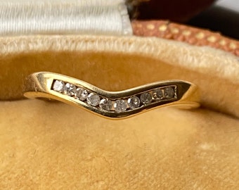 Op de afbeelding: Een gouden band met een rij kleine diamanten die in een gebogen, V-vormig ontwerp zijn gezet.