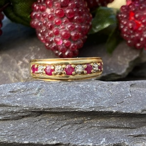 May include: A gold band ring with a row of red rubies and small diamonds set in the band.